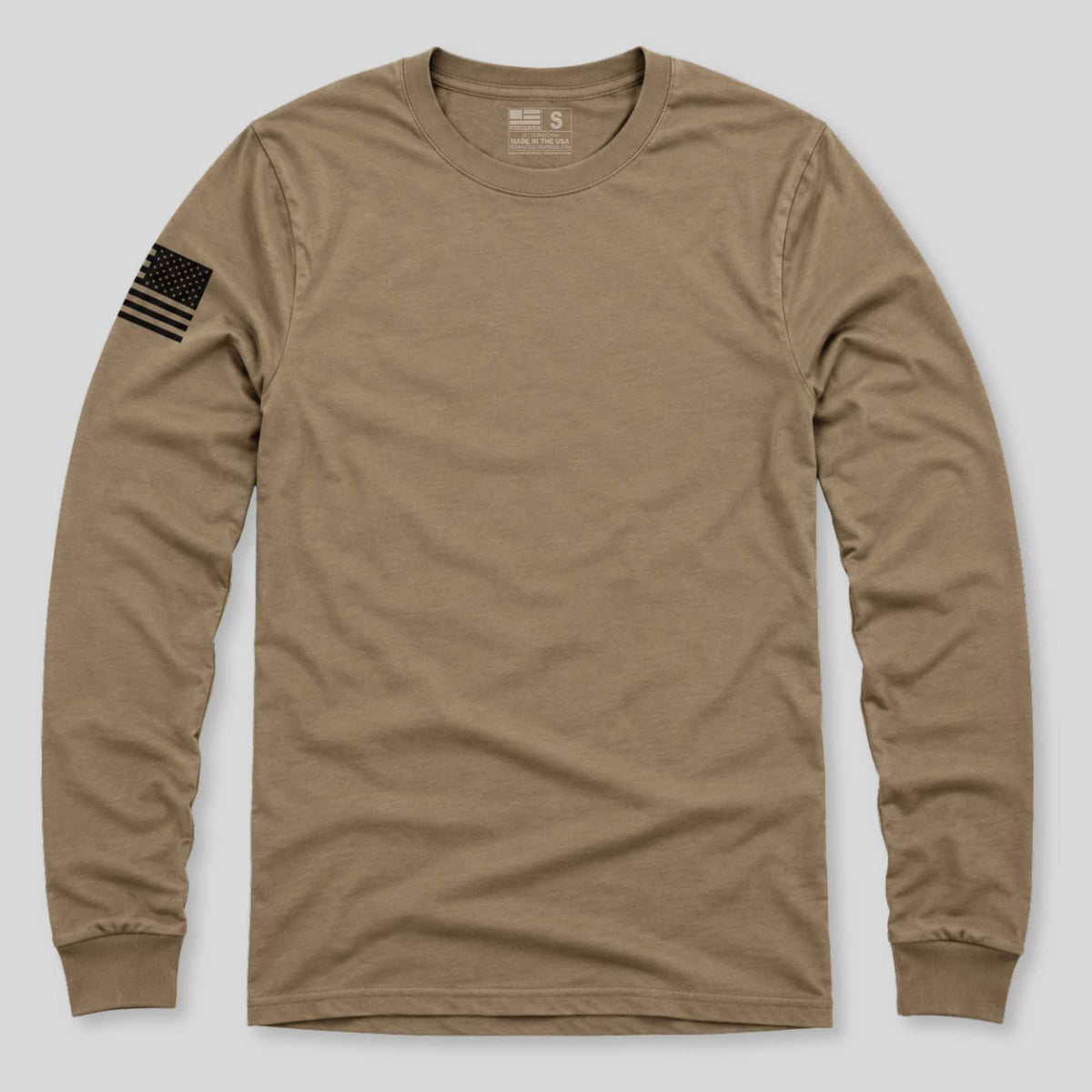 A tan long-sleeve crewneck t-shirt with a black American flag graphic printed on the left sleeve, displayed flat against a light gray background.