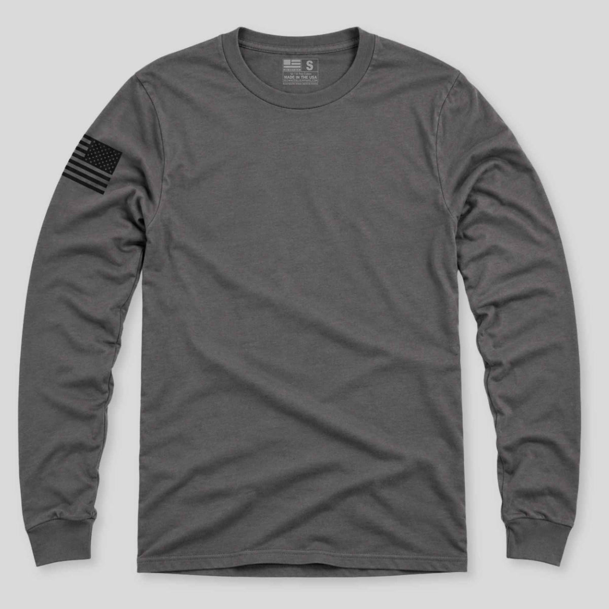 A dark gray long-sleeve crewneck t-shirt with a black American flag patch on the left sleeve, displayed flat against a light gray background.