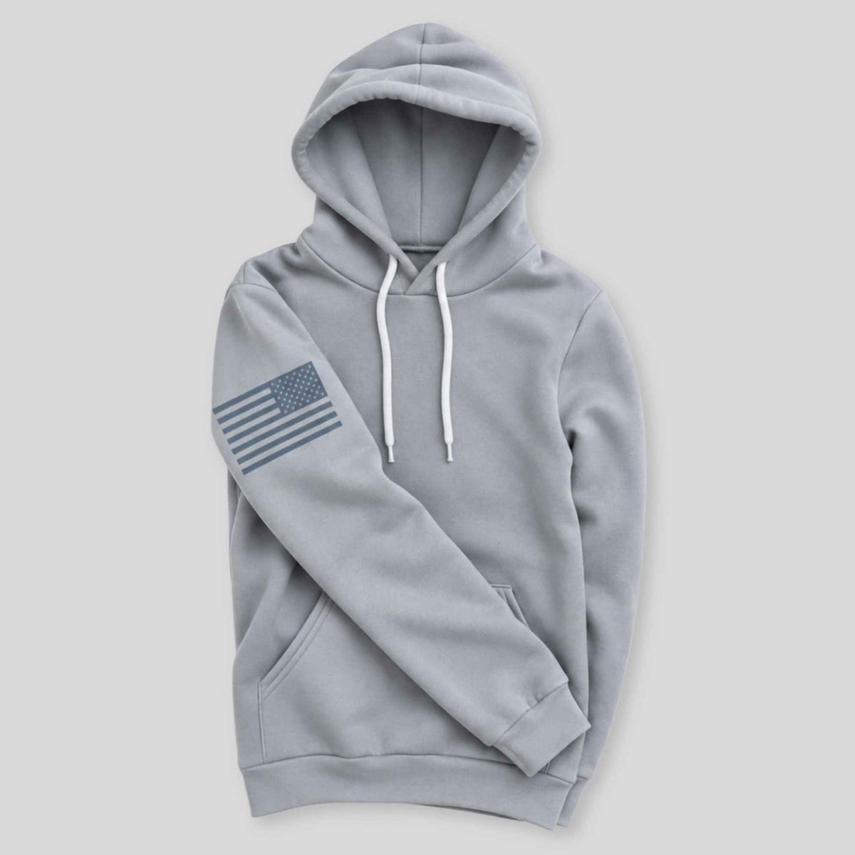 A light gray pullover hoodie with white drawstrings and a dark gray American flag graphic printed on the left sleeve, displayed against a solid light gray background.