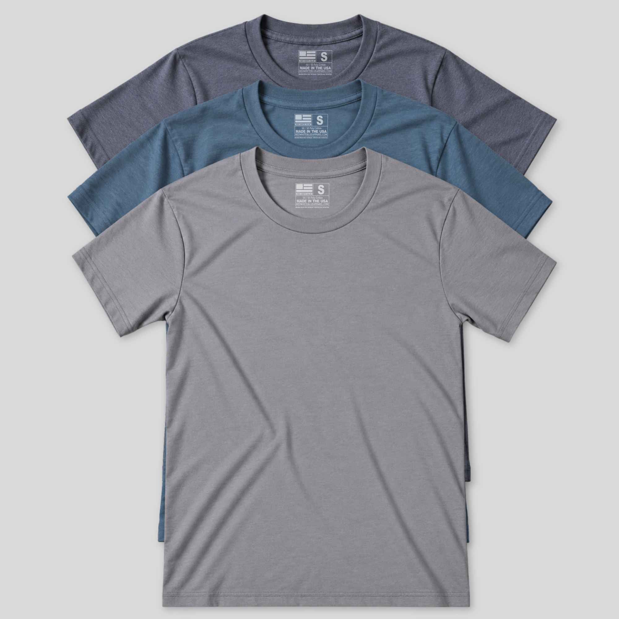 Three short-sleeve Made In USA crewneck t-shirts in heather gray, slate blue, and charcoal gray, arranged in a stacked fan layout on a light gray background.