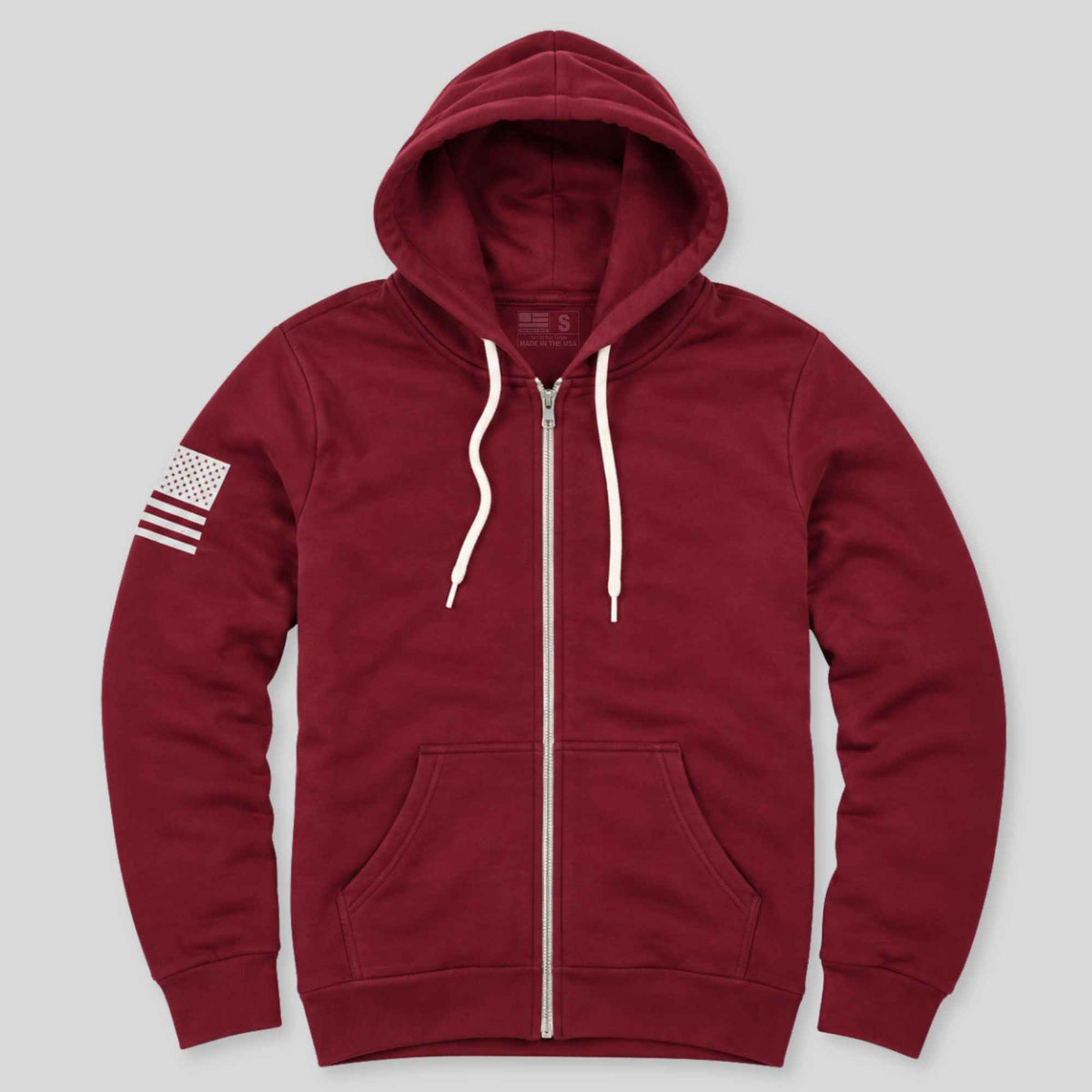 A maroon zip-up hoodie with white drawstrings, a front kangaroo pocket, and a white American flag graphic on the left sleeve, shown against a light gray background.